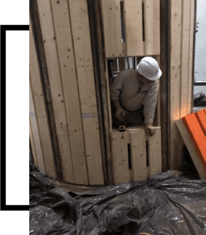 A man in white hard hat looking out of a hole.